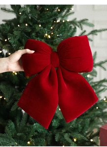 Close-up of a large red velvet Christmas bow being held against a glowing festive tree