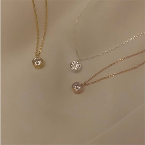 Detailed shot of gold, silver, and rose gold minimalist zircon necklaces on fabric