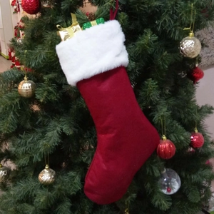 Chaussette de Noël rouge avec revers en peluche blanche suspendue sur un sapin décoré