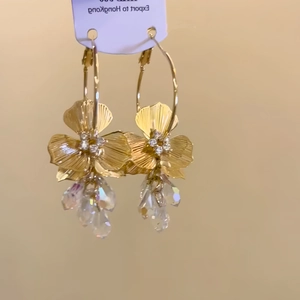 Gold plated floral drop earrings with clear crystal charms on a purple display card