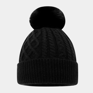 Detail einer schwarzen Strickmütze mit großem Kunstfell-Bommel und Zopfmuster-Struktur