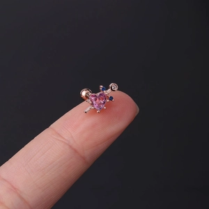 Close-up of a pink heart-shaped crystal ear stud on a fingertip showing micro size