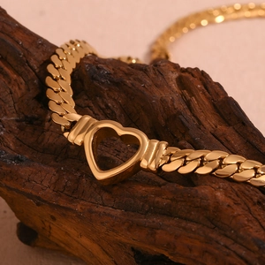 Macro detail of 18K gold-plated heart pendant and Cuban chain links on textured wood