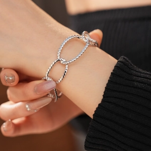 Close-up of a silver-tone hollow oval link bracelet with spiral texture on a wrist