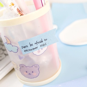 Close-up of translucent frosted pen holder with cute cartoon bear and blue sticky note