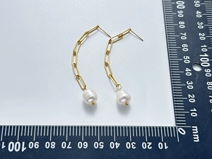Detail of elegant 18K gold-plated chain earrings with white freshwater pearls beside a ruler