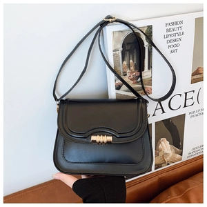 Gros plan sur un sac besace en cuir noir avec fermoir rotatif doré sur des magazines