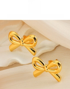 Detail of 18K gold bow stud earrings featuring a polished mirror finish on silk fabric