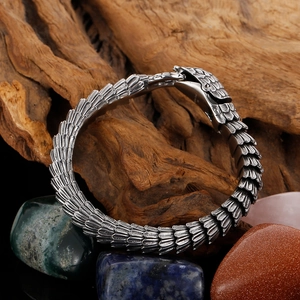 Detailed close-up of silver snake scale texture bracelet on natural wood with stones