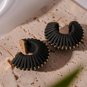 Detail shot of black textured C-shape earrings with gold metallic beads on travertine
