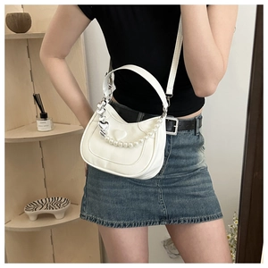 Detailed view of white crescent bag with pearl chain and silver heart charm decoration