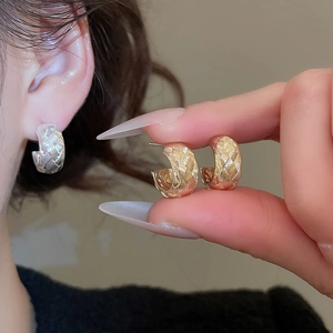 Detail of C-shaped metal earrings featuring a textured woven pattern in gold and silver