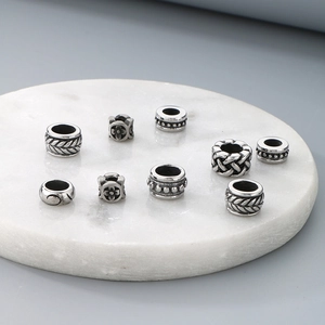 Nine vintage stainless steel beads with engraved patterns on white marble base