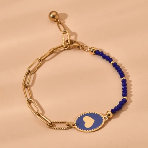 Golden chain bracelet with blue beads and heart oval pendant on beige backdrop