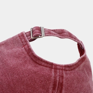 Detail of washed red baseball cap showing adjustable metal buckle and vintage cotton texture