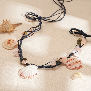 Bohemian woven raffia necklace with natural sea shells on a beach sand background