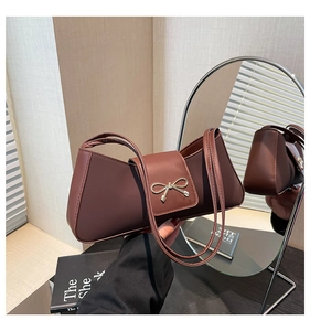 Detail of dark brown baguette bag with gold bow clasp and elegant shoulder straps
