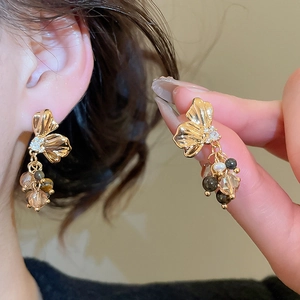 Detail of golden petal earrings with zircon and colorful beads on elegant female model