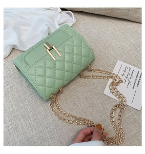 Detail view of mint green quilted chain bag with gold metal lock on a textured surface