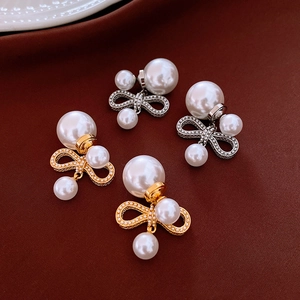 Detailed view of gold and silver bow pearl earrings displayed on textured fabric