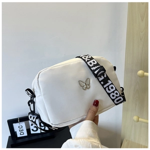 Close-up of white nylon crossbody bag with silver butterfly and wide lettered strap