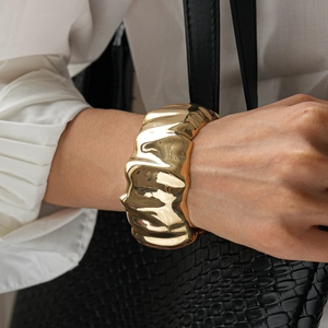 Detail of wide gold irregular pleated resin bangle styled with white pleated shirt