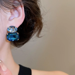 Close-up of geometric gold earrings with oval light blue and rectangular dark blue stones