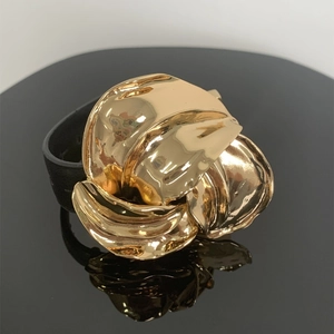 Macro-opname van goudkleurige metalen bloem op zwart leren band met spiegelreflectie
