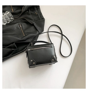 Detail view of black box cross-body bag featuring silver studs and industrial zip accents