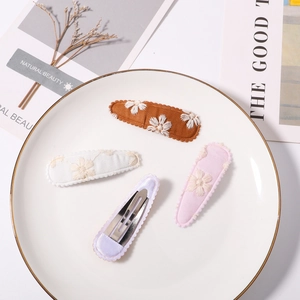 Close-up of four floral embroidered snap hair clips in diverse pastel colors on a ceramic tray