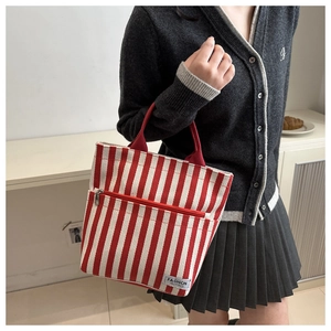 Detail of red striped canvas tote bag featuring front zipper pocket and fashion logo label