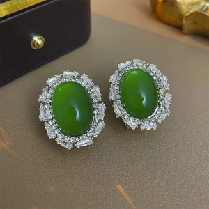Detail view of retro oval green emerald earrings with radial zircon setting on a brown surface