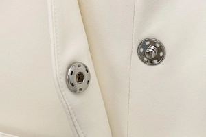 Detailed macro view of the metal snap button on an elegant cream-colored belted blazer