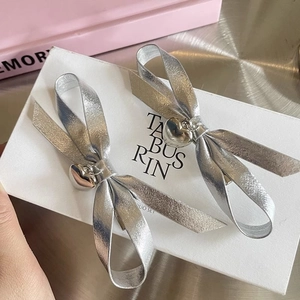Detail view of two silver ribbon bow hair clips with heart charms on a white gift box