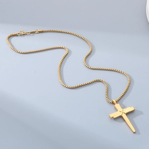 Vue de dessus d'un pendentif croix en acier titane doré sur une chaîne à mailles carrées
