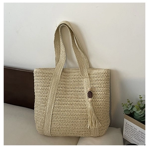 Close-up of beige woven straw tote bag featuring detailed texture and tassel with wood bead