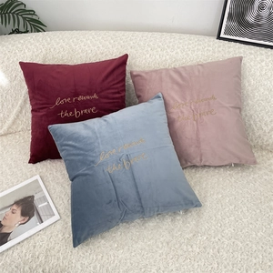 Close-up of velvet pillows with gold 'Love rewards the brave' embroidery in assorted colors