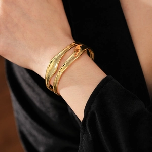 Detail of irregular double-layer gold wave cuffs with a hammered texture on wrist