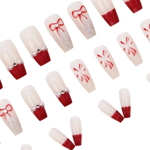 Détail de faux ongles coffin avec nœud rouge, perles et touches de paillettes argentées