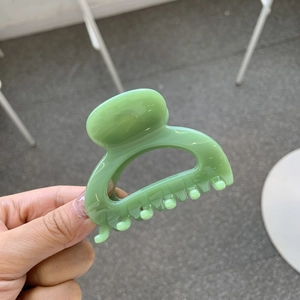 Detail of a light green glossy square hair claw clip held in hand with natural light