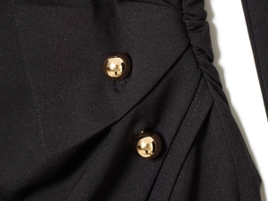 Nahaufnahme von elegantem schwarzem Strickstoff mit Falten und goldener Kugelknopfverzierung