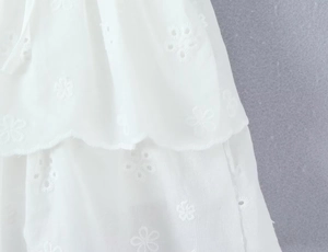 Detailed view of white floral embroidery lace and tiered ruffle layers on cotton fabric