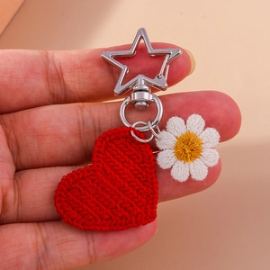 Knitted red heart and white daisy flower keychain with silver star clasp on palm