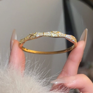 Detailed view of gold plated bangle with quilted pattern and cubic zirconia inlay
