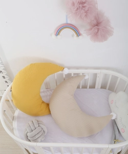 Detail of moon-shaped cotton nursing pillows with pom-poms in a wooden crib