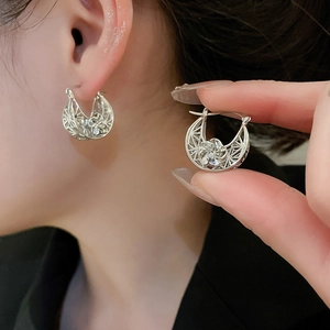 Macro detail of silver hollow flower hoop earrings worn on model for retro style