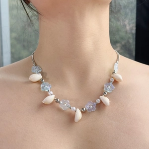 Close-up of summer necklace with white shells, blue flower beads and pearls on model