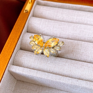 Close-up of yellow marquise-cut zircon butterfly ring on a cream fabric jewelry box
