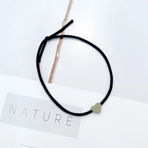Detail showing a black elastic hair tie with a small green heart pendant on a nature backdrop