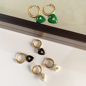 Three pairs of heart-shaped drop earrings in green, black and white on mirror surface